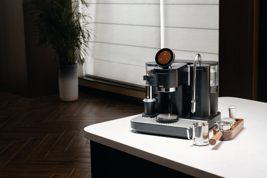 Meraki Espressomaschine mit rundem Display und Dampflanze neben Milchkännchen und Tamper vor einem hellen Fenster.