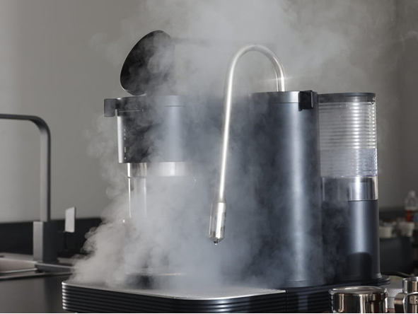 Schwarze Meraki Espressomaschine mit sichtbarer Dampfwolke rund um die Dampflanze.
