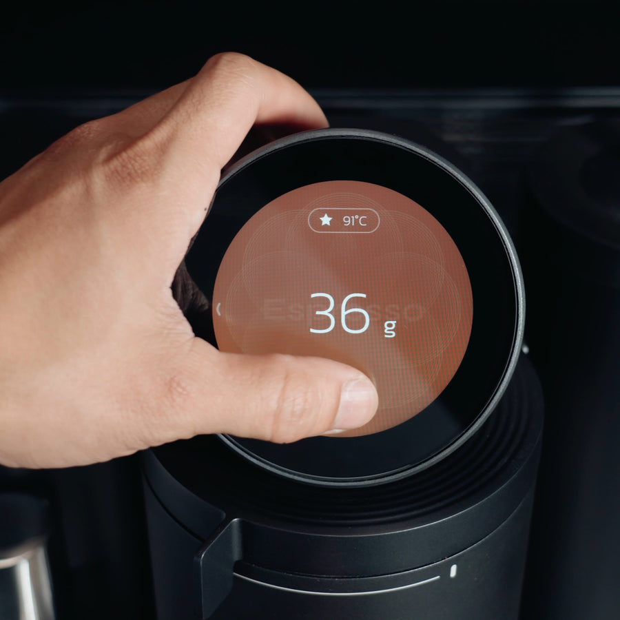 Hand am runden Display der Meraki Espressomaschine mit angezeigten Einstellungen von 36 g und 91 °C.