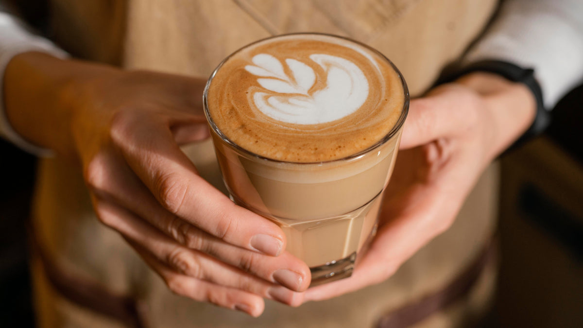 Hände halten ein frisch zubereitetes Latte-Art-Kaffeegetränk im Glas
